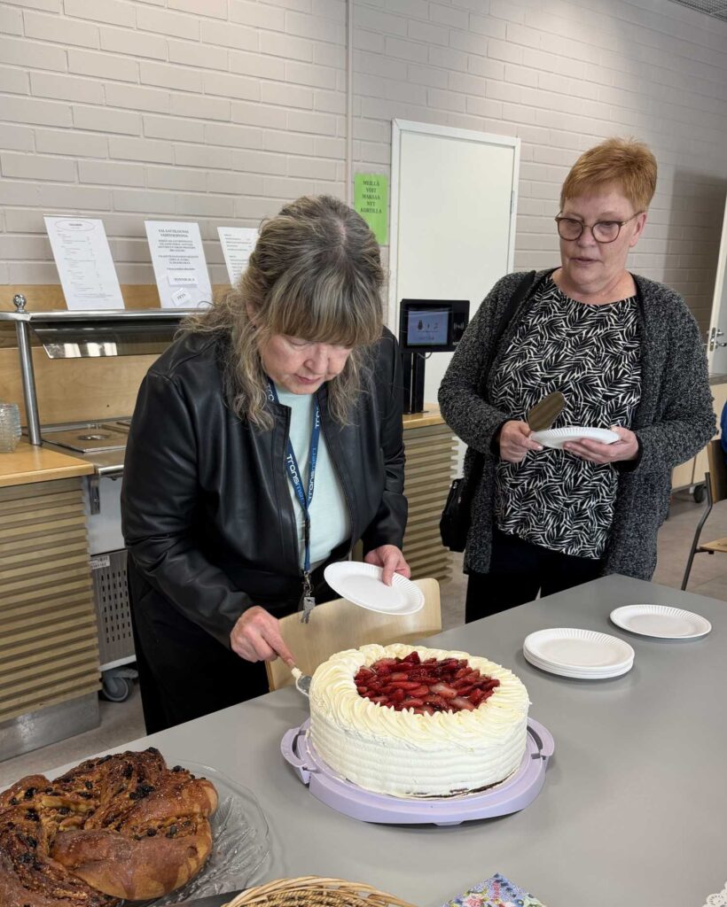 Anneli leikkaamassa mansikkakakkua. Annika odottaa vuoroaan.